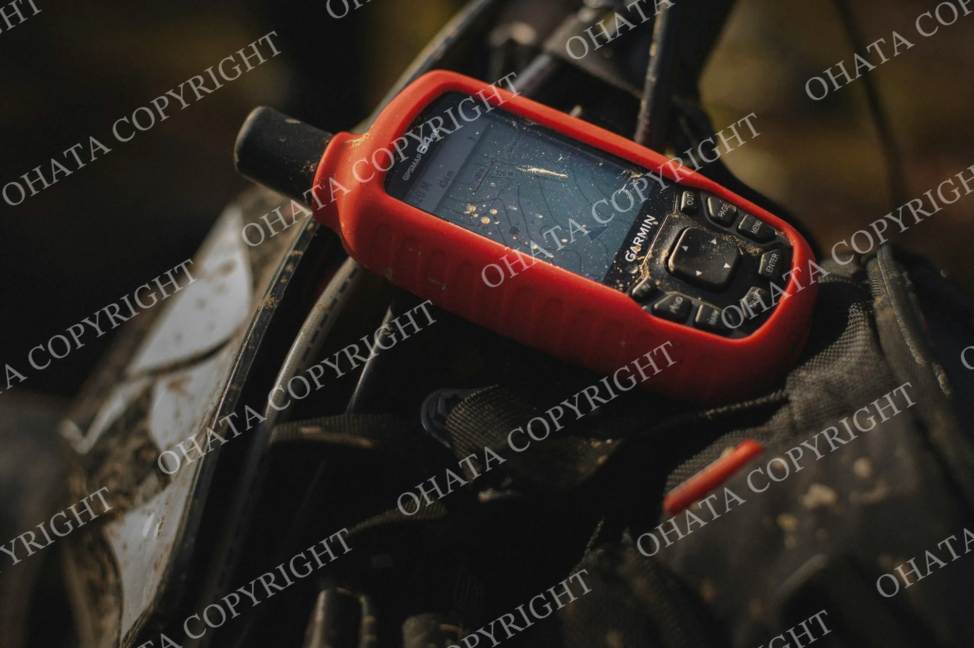 Garmin handheld GPS receiver in a red protective cover resting on outdoor equipment.