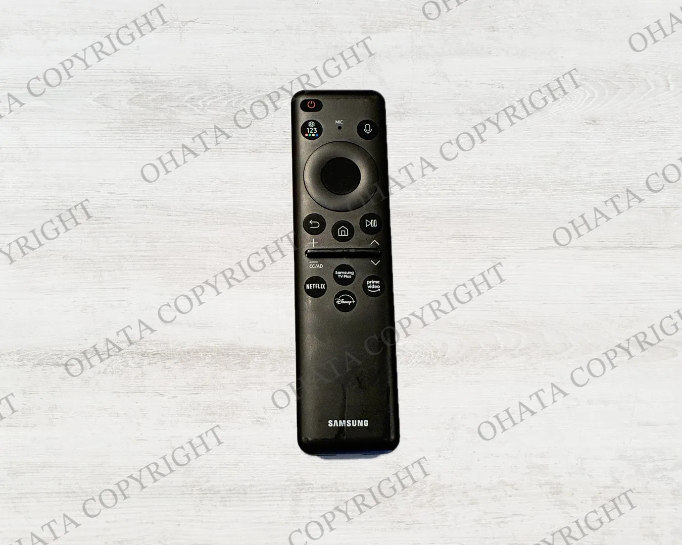 Black Samsung television remote with a circular navigation pad, microphone button, and streaming shortcut buttons.