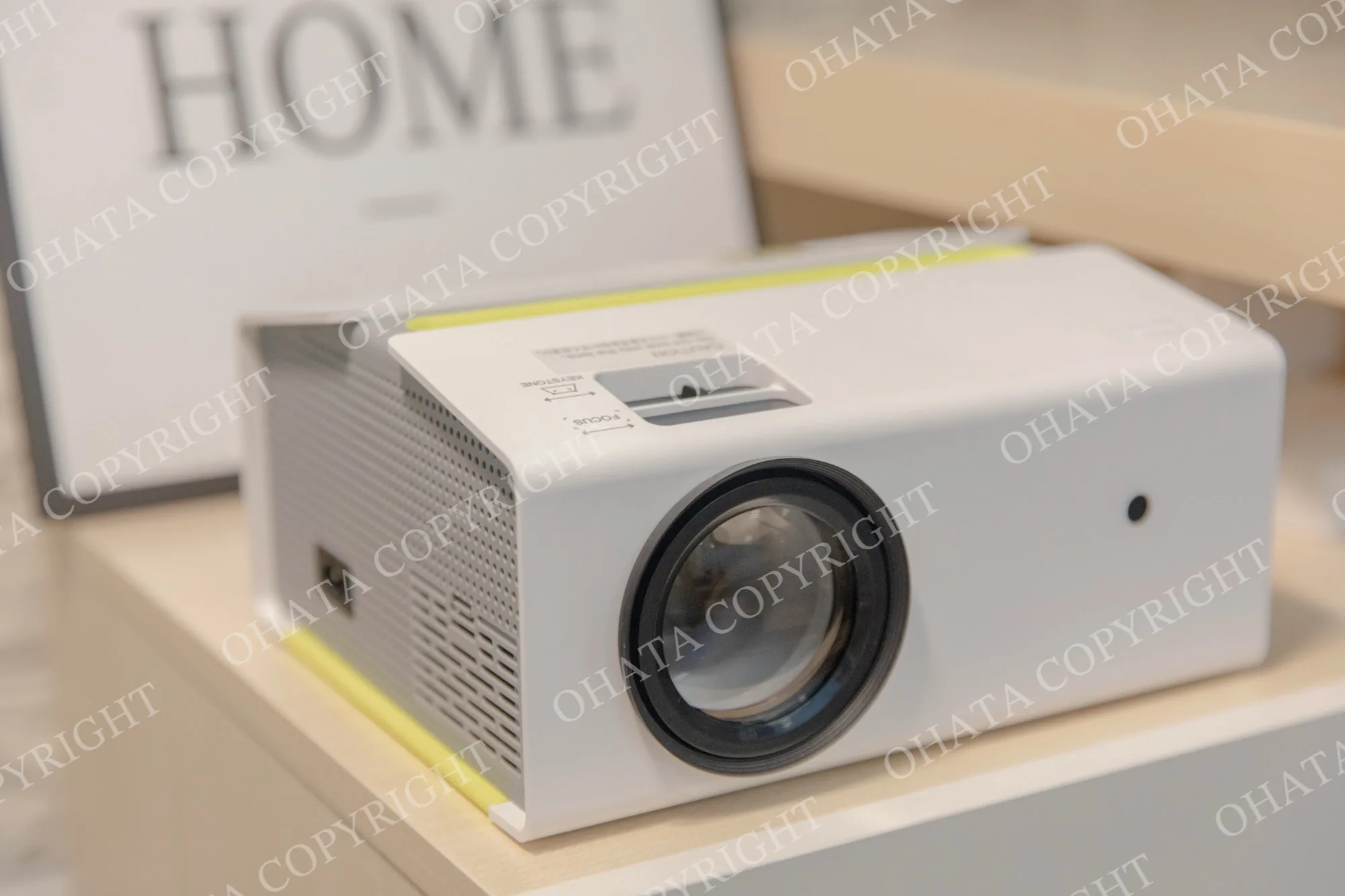 White video projector on a shelf with a front lens and side ventilation grille.