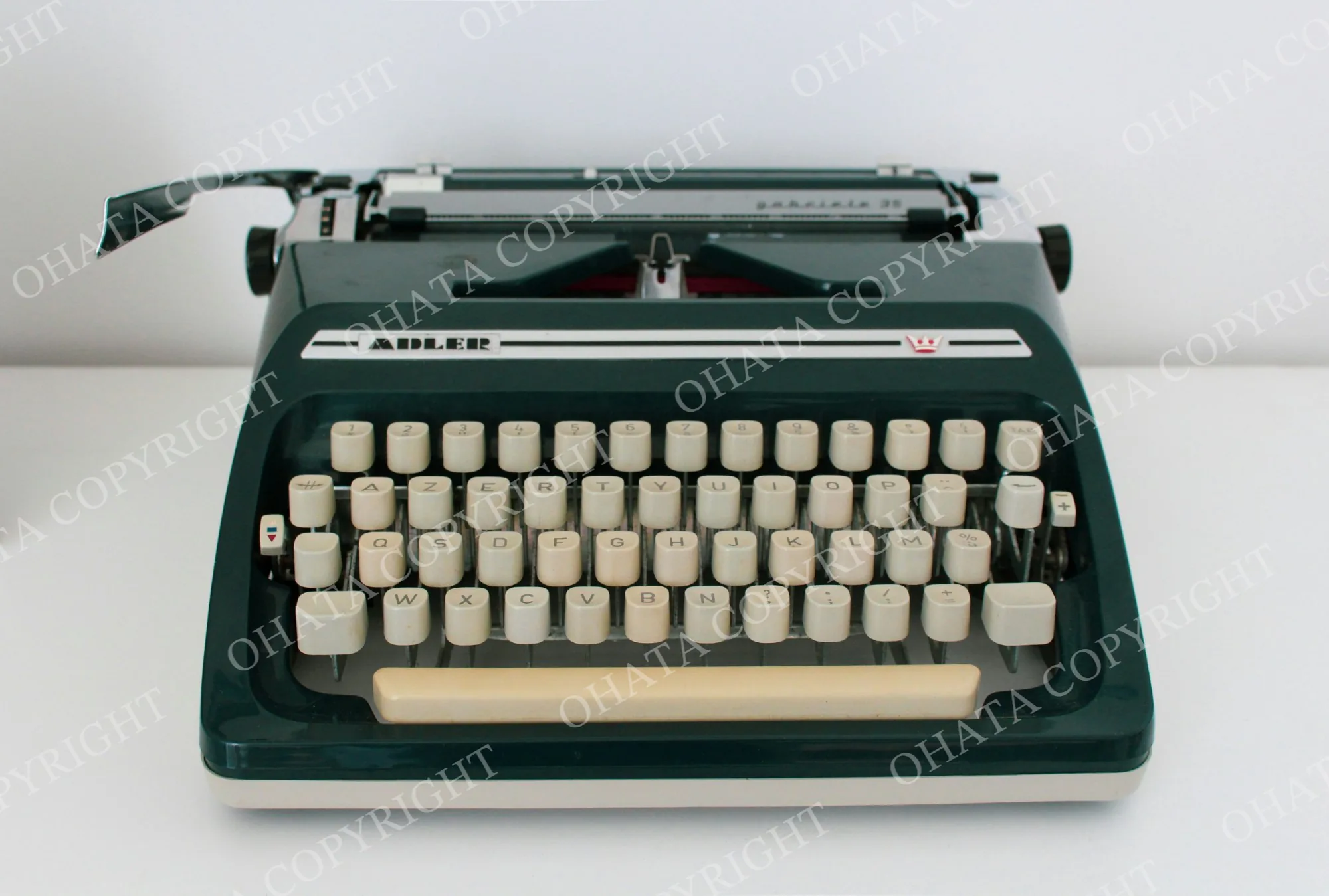 Green and cream Adler manual typewriter with a visible keyboard, paper carriage, and carriage-return lever.