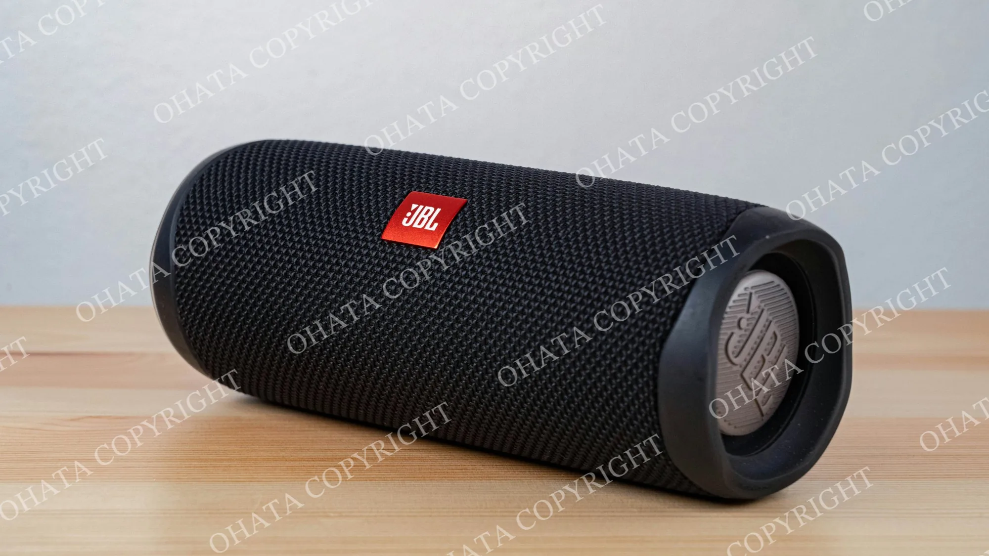 Black cylindrical JBL portable speaker resting on a wooden surface.