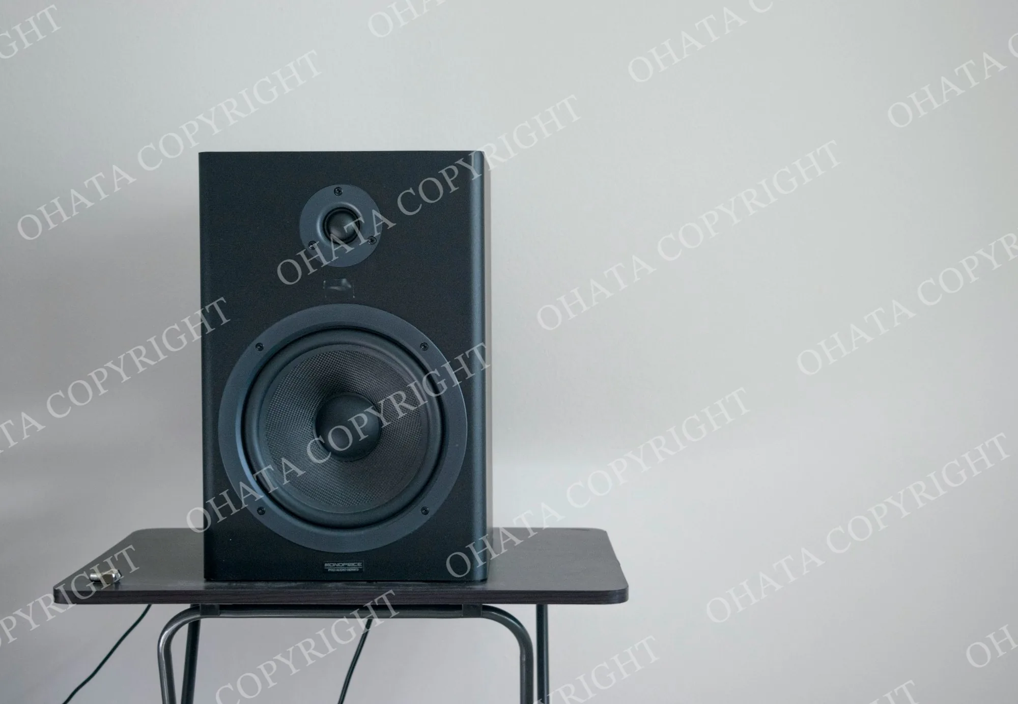 Black speaker cabinet with a tweeter and larger woofer, standing on a small table.