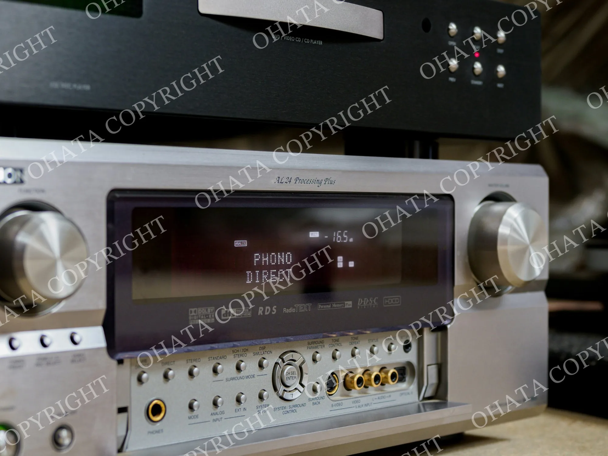 Silver AV receiver with a front display, control knobs and audio-video connections, beneath a separate disc player.