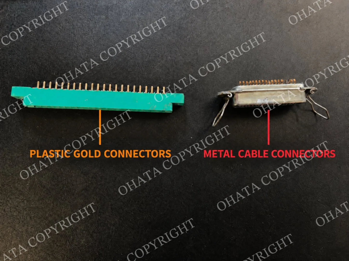 Green plastic connector and silver metal cable connector displayed side by side on a dark surface with orange and red identification labels.