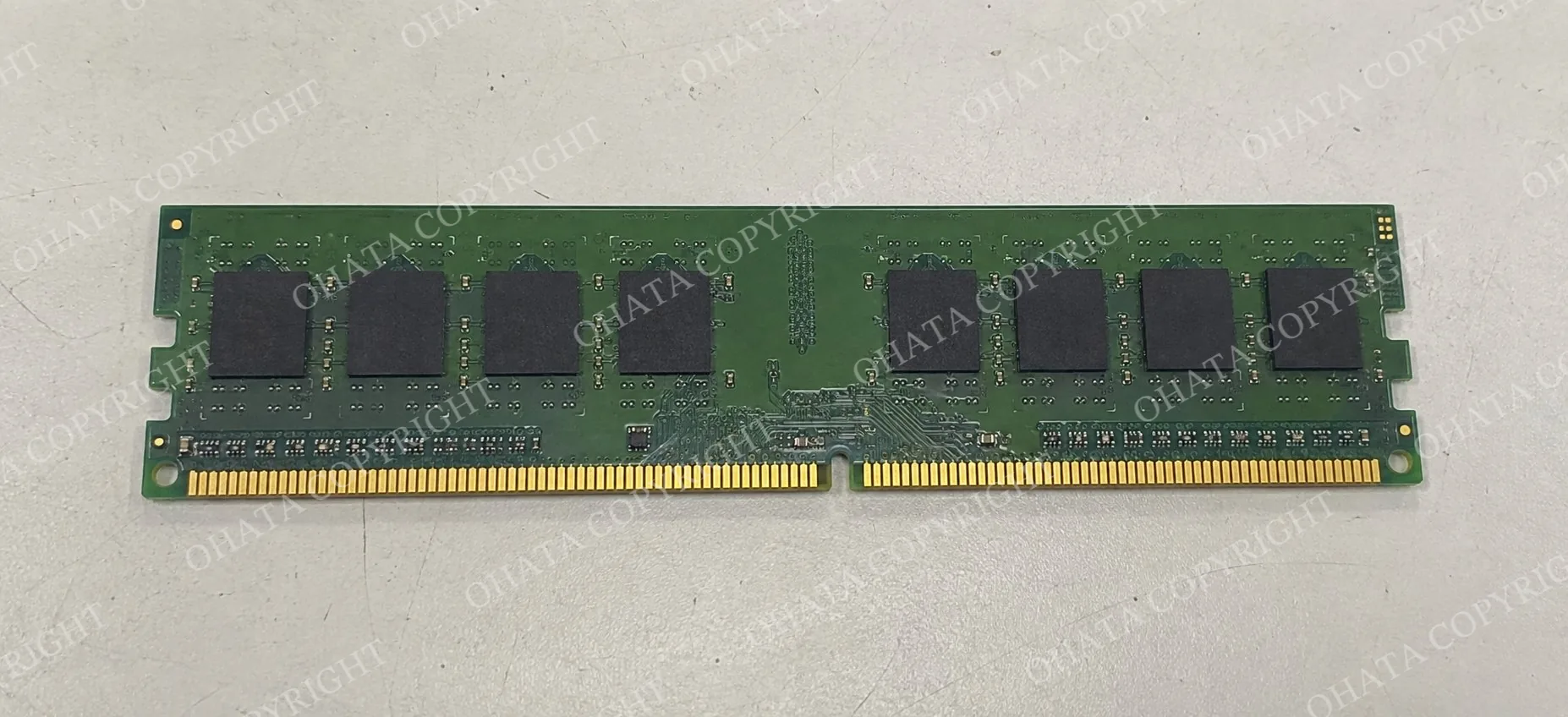 Top-down view of a green RAM module with intact gold fingers and a central alignment notch on a white-gray worktable.