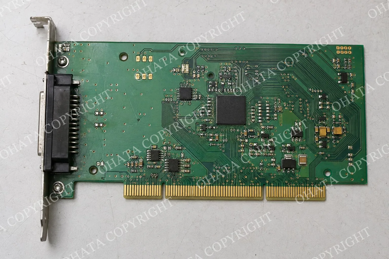 Top-down close-up of a green circuit board with long gold fingers along its edge and smaller gold-colored pads elsewhere on the board.