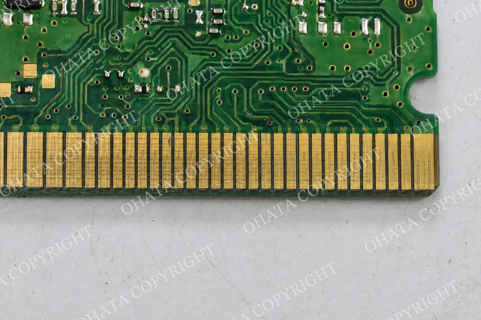 Top-down macro view of used gold fingers with fine parallel contact marks on a green circuit board resting on a white-gray worktable.