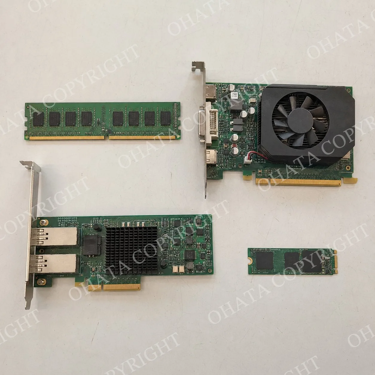 Top-down arrangement of a RAM module, graphics card, expansion card, and M.2 module with visible gold fingers on a white-gray worktable.