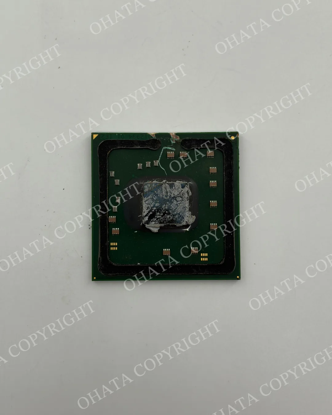 Top view of a removed green BGA chip with an exposed central die covered in thermal-paste residue.