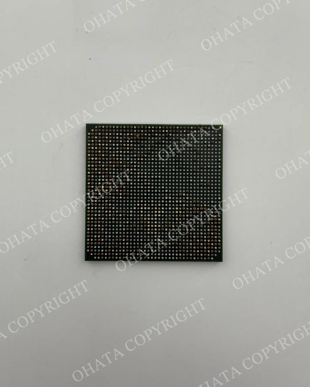 Underside of a removed green BGA chip showing a dense grid of solder balls, with some contacts flattened or missing.