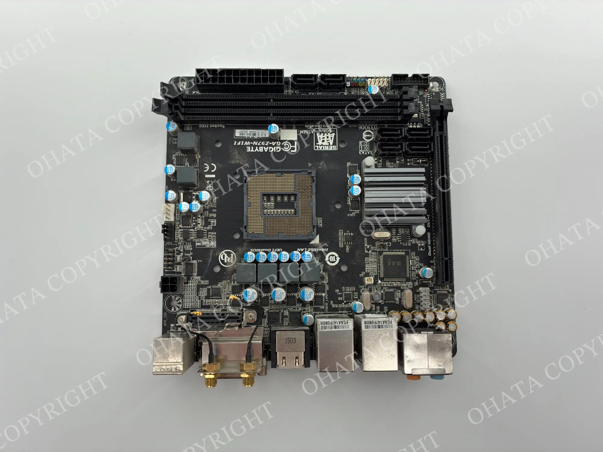 Front view of a compact GIGABYTE desktop motherboard with an empty CPU socket, memory slots, connectors, and attached heat sinks.