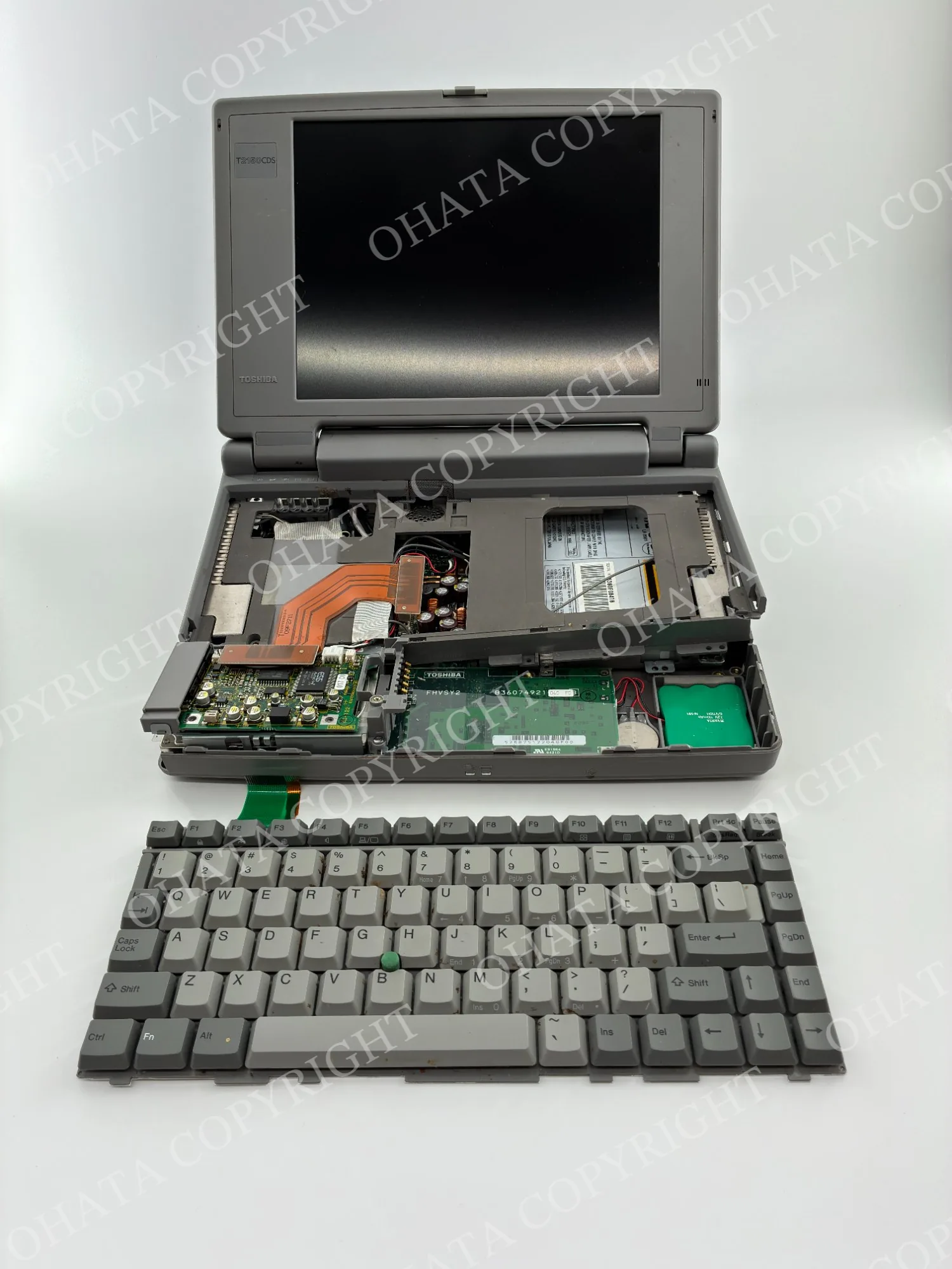 Partially dismantled Toshiba laptop with its keyboard removed and internal circuit boards and cooling system exposed.