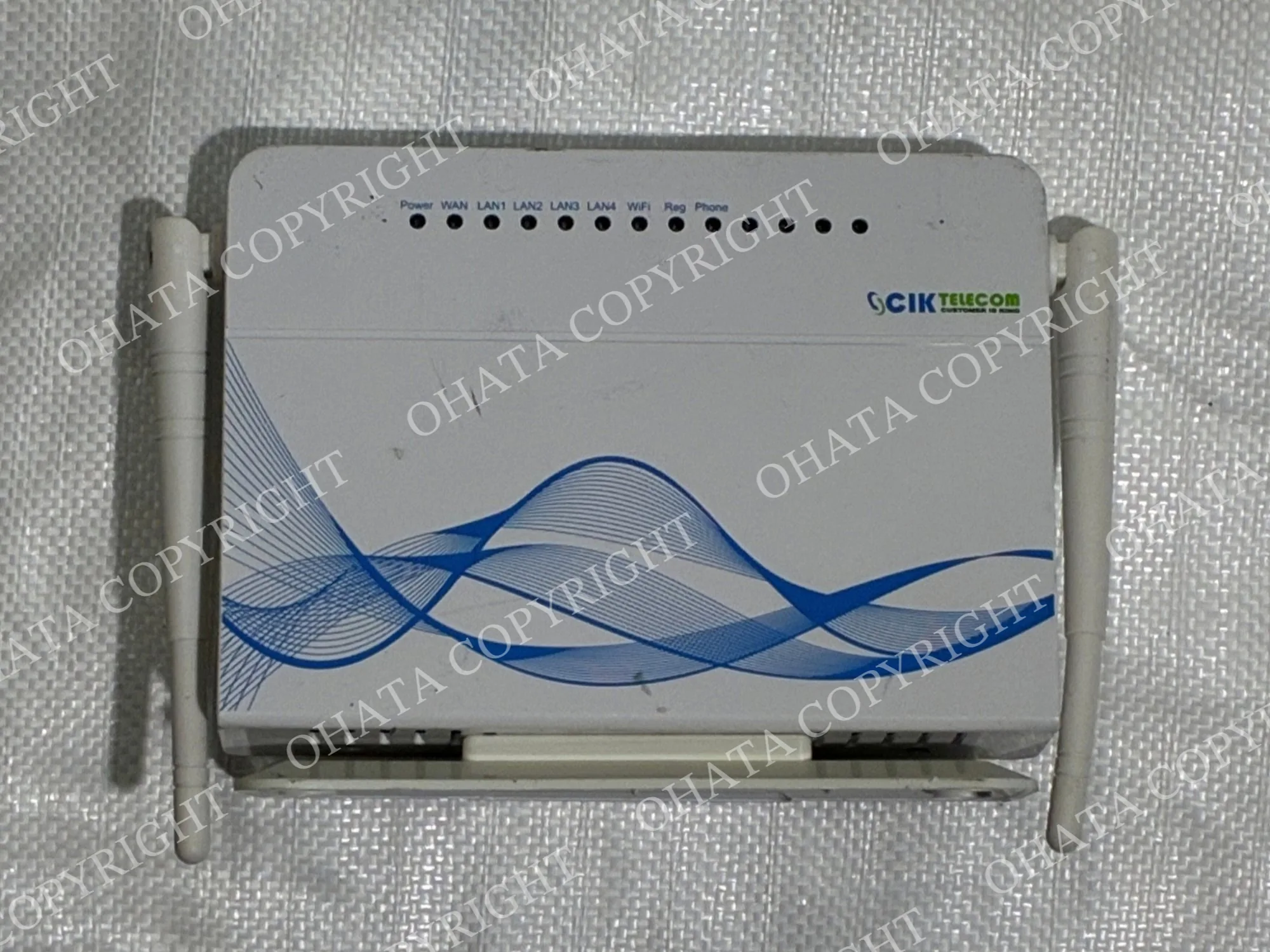 White CIK Telecom wireless router with two external antennas, front status lights, and a blue wave design across the housing.